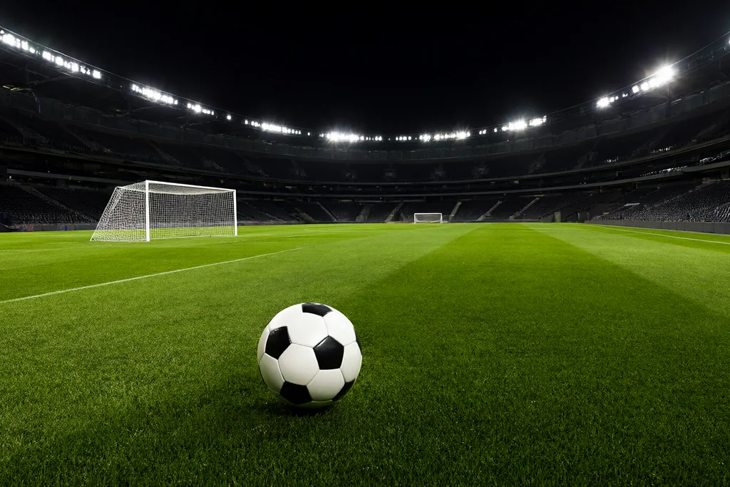 Estádio iluminado visto das arquibancadas vazias à noite com gramado verde