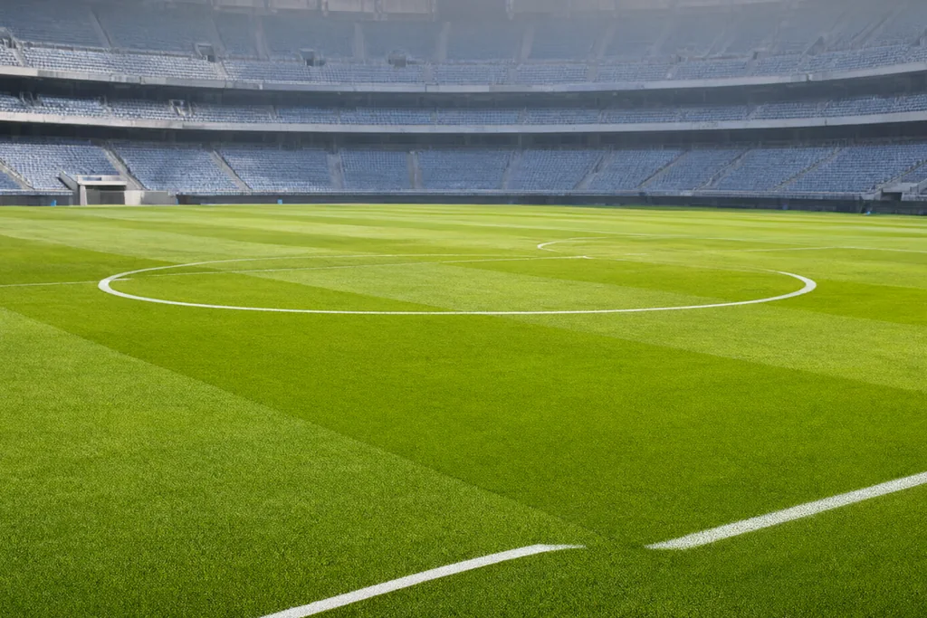 Campo de futebol de um estádio vazio visto do alto das arquibancadas, com o círculo central